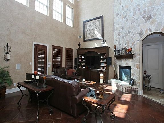 Large family room with tall ceilings, stone wall, stone floors, plantation shutters, built-ins, and bright tall windows.