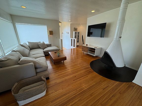Open living room with mid-century freestanding fireplace, large sectional, and hardwood floors throughout.
