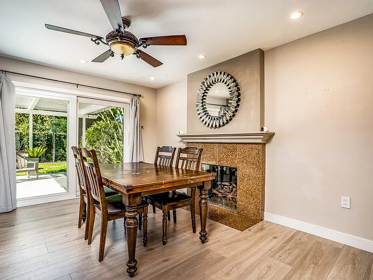 Dining room has ceiling fan and fireplace with granite hearth. The large sliding patio door opens out to lush green garden.