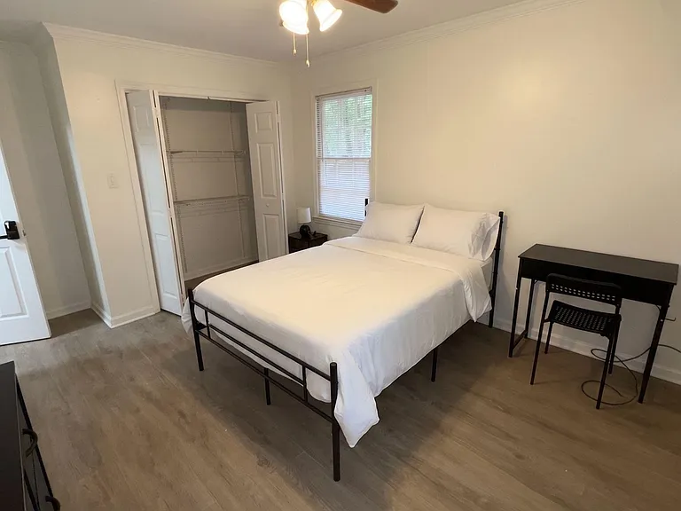 Furnished bedroom with a ceiling fan, window with blinds, open closet shelving, and a dedicated desk workspace.