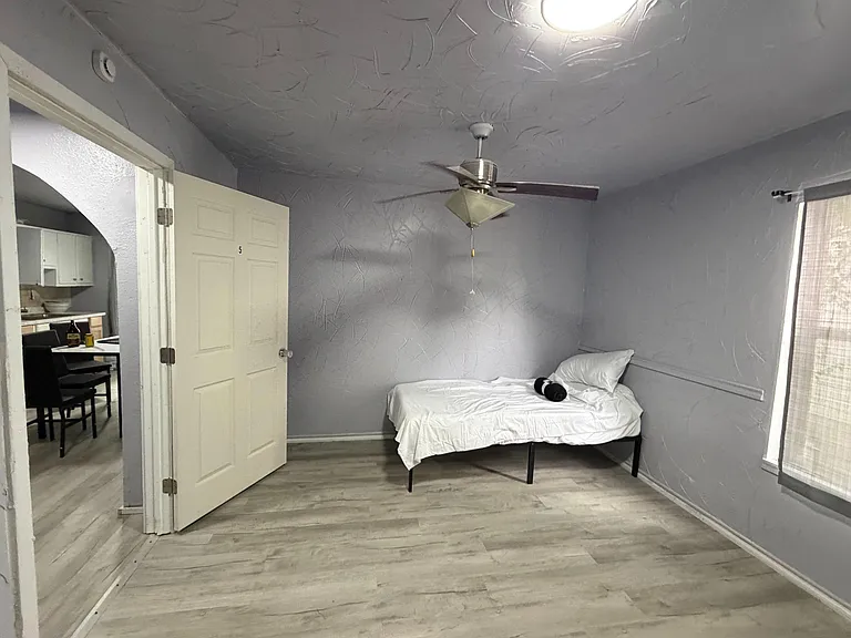 Private bedroom with durable plank flooring, ceiling fan, and a window with blinds; convenient access to shared areas.