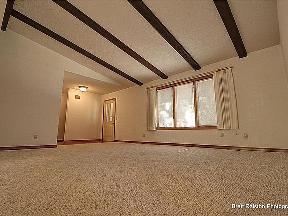 Another view of entry and living area. Gorgeous beamed ceiling. Wood casement windows with blinds. Durable berber carpet in neutral color keeps room bright and allows beams to POP!