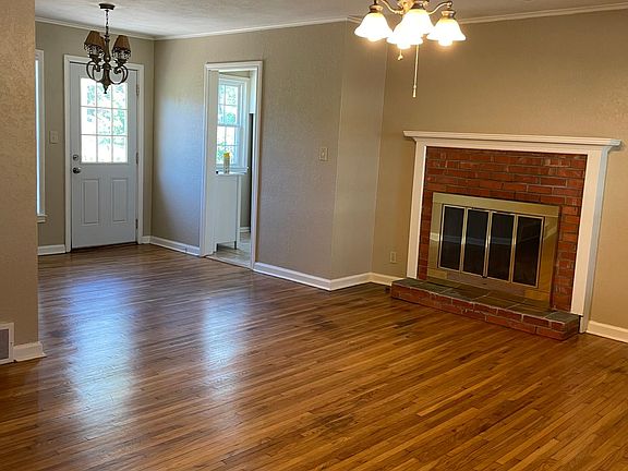 Living room with blinds, ceiling fan and fireplace opens to dining room.