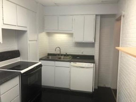 Black countertops with exposed brick and plenty of cabinets. Dishwasher, double-sided sink, glass top stove.