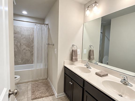 Hall bathroom with a double-sink vanity, cabinet storage, and tub/shower combination.