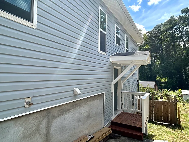 To the right of the house, you'll find a wooden back porch. The green space of the backyard is enclosed by wooden fencing. This wooden gate is one of two entrances to the backyard.
