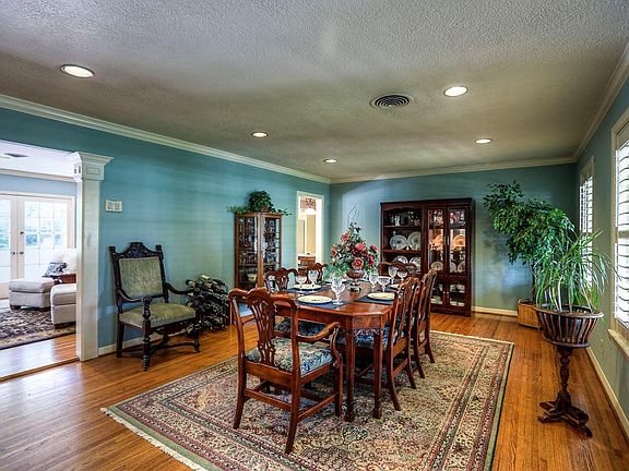 The dining room flows seamlessly through the columned passageway into the living room and both look out at the verdant yard.
