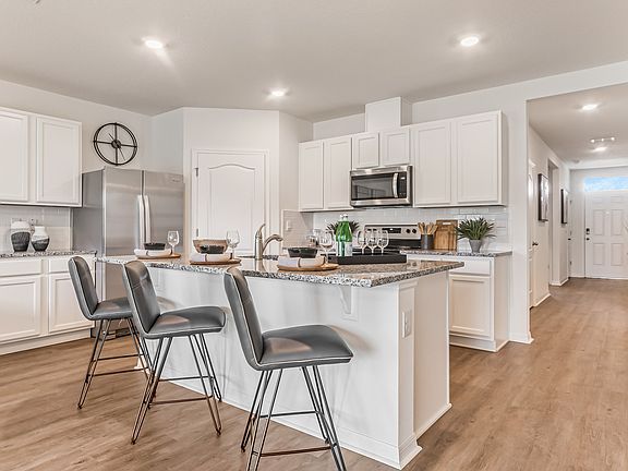 St. Cloud, FL, Homes for Rent - Ibis Park at Harmony West - Chef-Inspired Kitchen with Luxury Vinyl Plank Flooring, Island with Bar-Style Chairs, Granite Countertops, and Stainless-Steel Appliances.