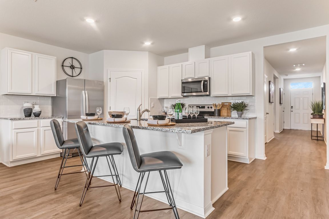 St. Cloud, FL, Homes for Rent - Ibis Park at Harmony West - Chef-Inspired Kitchen with Luxury Vinyl Plank Flooring, Island with Bar-Style Chairs, Granite Countertops, and Stainless-Steel Appliances.