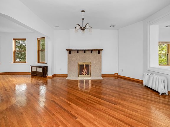 This expansive living room features a charming decorative fireplace, abundant sunlight, and beautiful hardwood floors, creating a warm and inviting atmosphere.
