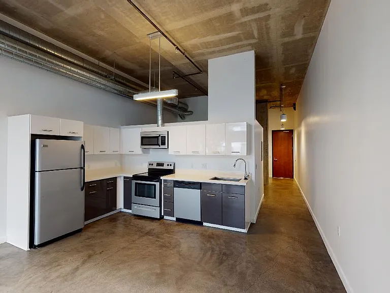 Apartment kitchen with stainless steel appliances, quartz countertops and polished concrete flooring.