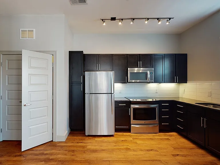 Apartment kitchen with stainless steel appliances, granite countertops and wood-style flooring.