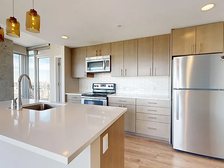Apartment kitchen with stainless steel appliances, quartz countertops and wood-style flooring.