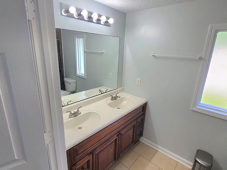 Bathroom with dual-sink vanity, large mirror, and frosted window for privacy, plus ample counter and cabinet storage.