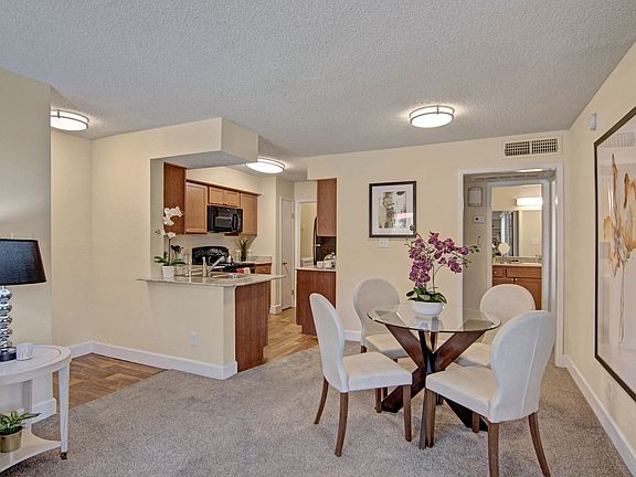 A living room with a view into the kitchen and overhead lighting