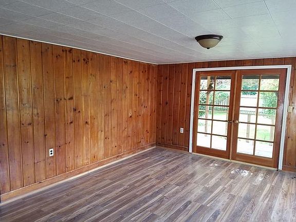 Knotty pine planked walls in living room with french door leading to the front porch and fenced yard
