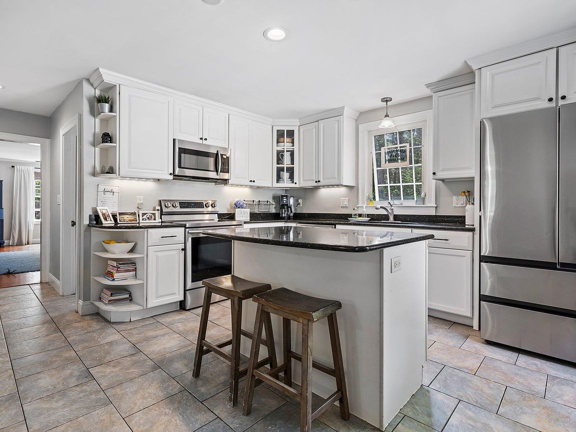 Updated white kitchen with granite counters, a large center island with bar stools, and stainless steel appliances at 26 Garrison Lane in Hopkinton NH