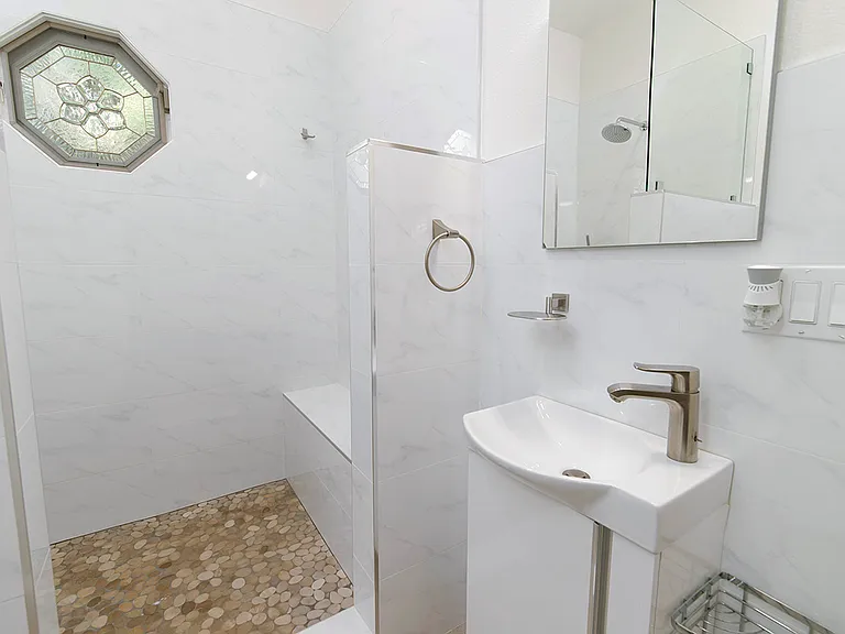 Ensuite vanity with small sink cabinet and step-in shower that has seating bench.