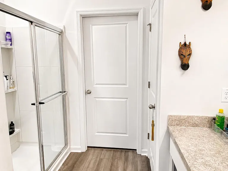 Clean full bathroom with a glass-enclosed shower, built-in shelving, and a long vanity counter for daily storage.