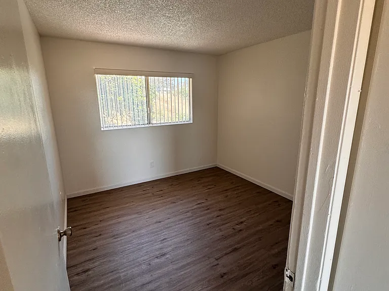 Bright bedroom with large window and wood flooring.