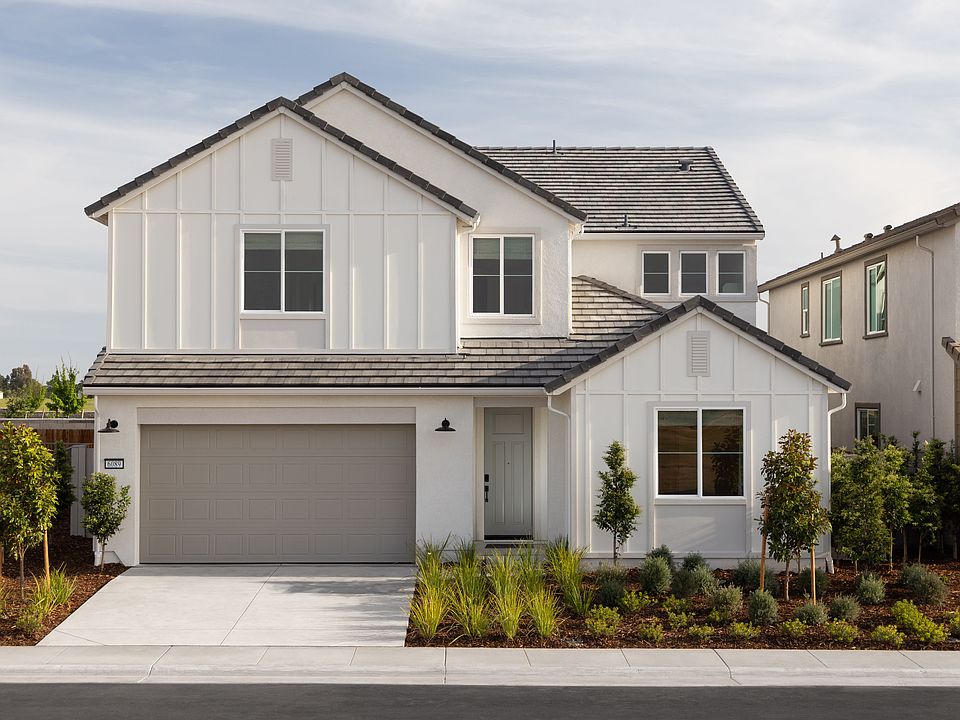 A two-story white house with a gray roof, surrounded by landscaped greenery, stands in the foregroun