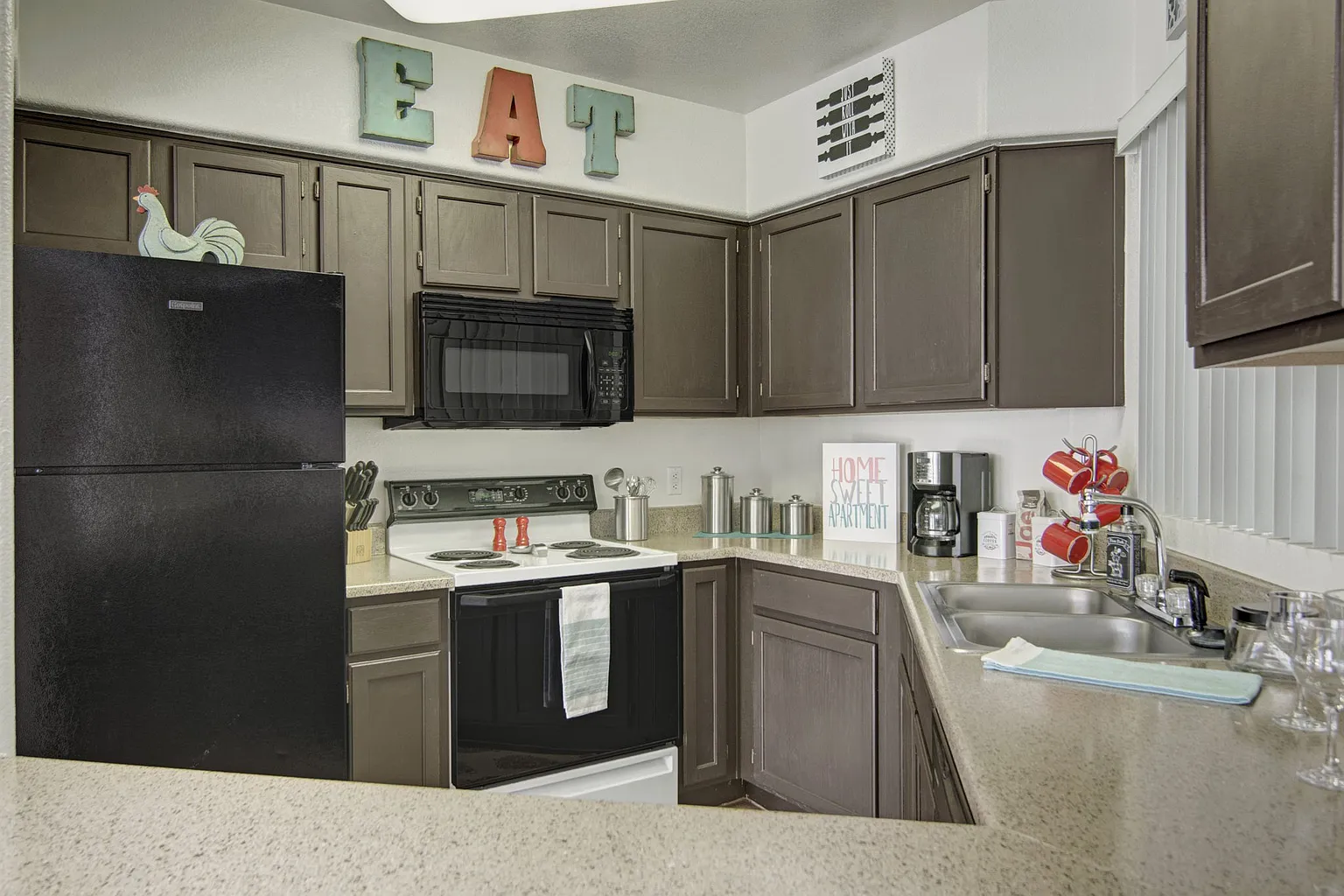 Kitchen with dark cabinets, a black refrigerator, white stove, and microwave. "EAT" decor above cabinets.