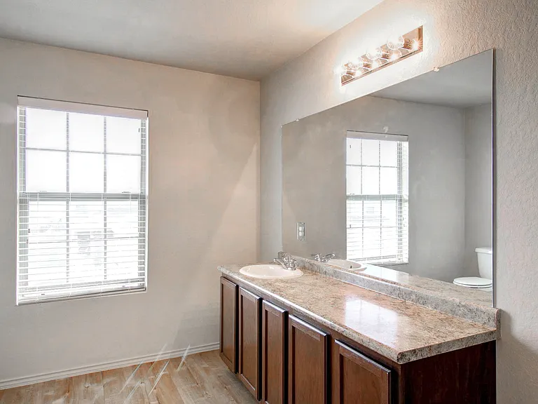 Elegant bathroom with dual sinks on a granite countertop, large mirror, and natural light from a window with blinds. Elegant bathroom with dual sinks on a granite countertop, large mirror, and natural light from a window with blinds.