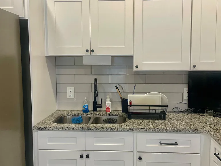 Kitchen workspace with shaker cabinets, granite-look counters, and a double-basin sink with subway-tile backsplash.
