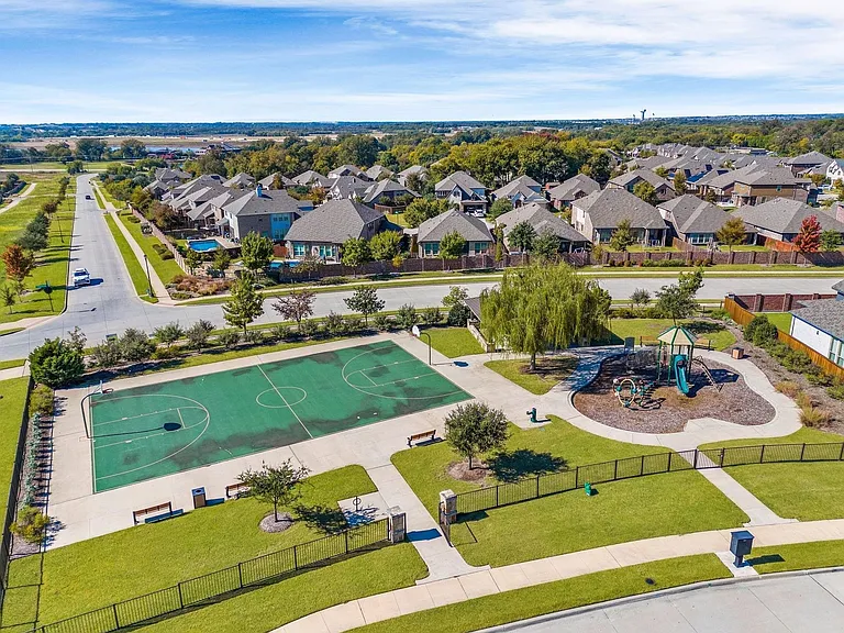 Community recreation area featuring a basketball court, playground equipment, mature trees, and landscaped grounds