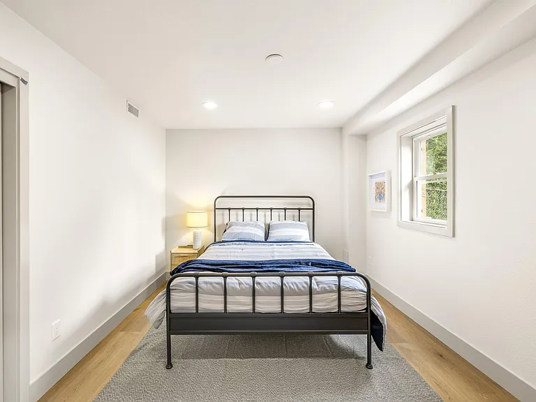 Well-sized bedroom with a full bed, nightstand lighting, and a large window for natural light and fresh air.