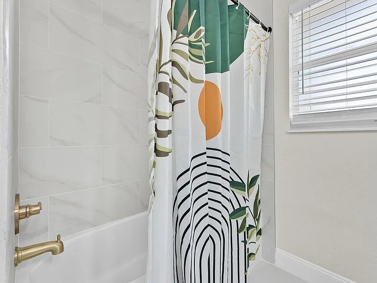 Tiled tub/shower combo with a window and blinds for ventilation and natural light, plus updated fixtures for daily use.