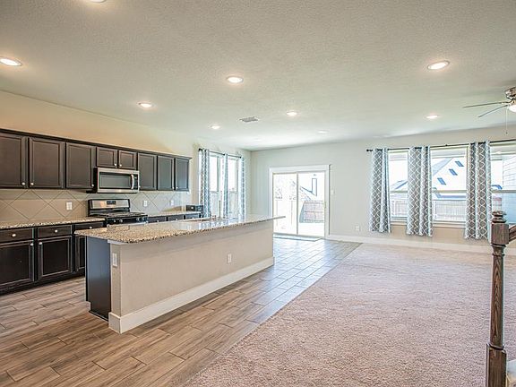 Kitchen featuring tasteful backsplash, light stone countertops, appliances with stainless steel finishes, light hardwood / wood-style floors, and a kitchen island with sink