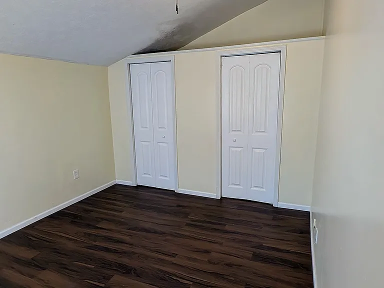 Spacious back bedroom featuring new dark wood-look flooring, ample closet space with double doors, and a modern ceiling fan beneath a vaulted ceiling.