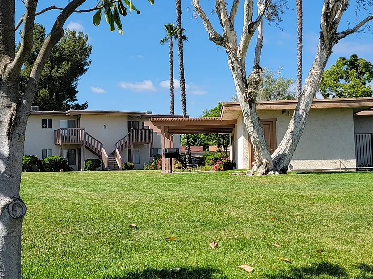 Nice grassy lawn area with pergola padio picnic area outside recreation center and swimming pool at Plaza Verde Apartments in Escondido, California.