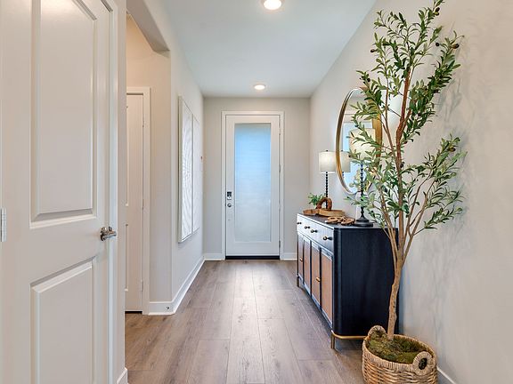 A bright and airy hallway with a wooden floor, a black cabinet, and a decorative plant arrangement,
