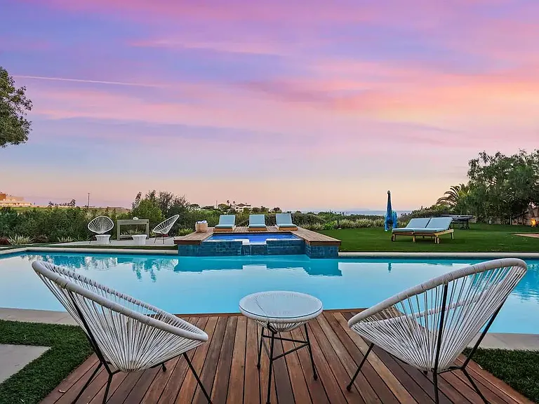 Chairs by the pool under a night sky painted with cotton candy hues.