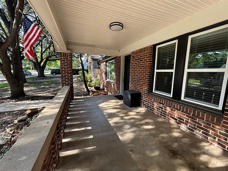 Covered concrete front porch featuring a brick facade, white trim, and a contemporary ceiling light fixture