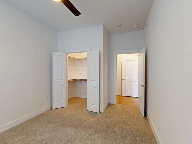 Spacious apartment bedroom with large closet and plush carpet flooring.