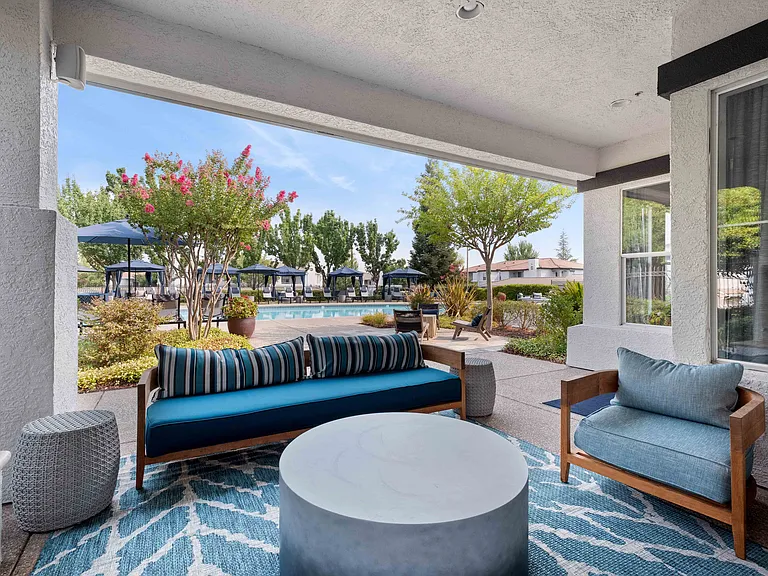 Our pool deck features a large sparkling pool, ample lounge seating, and a covered lounge with a cozy fire pit. Lush landscaping adds privacy and beauty between the pool and relaxation area.