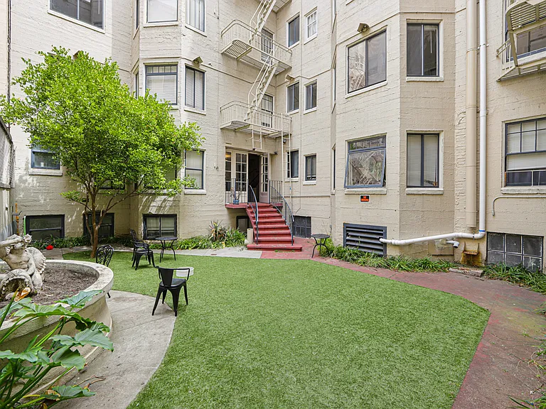 Courtyard with a fence, covered in lush green grass, and a brick walkway leads up to the entrance of the building