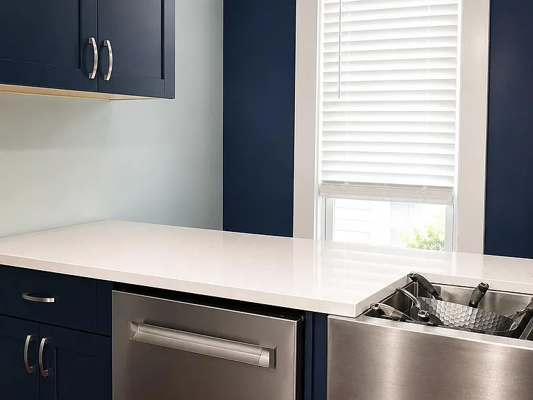 Kitchen with quartz countertops, stainless farmhouse sink and dishwasher, and ample cabinetry with a window over the sink.
