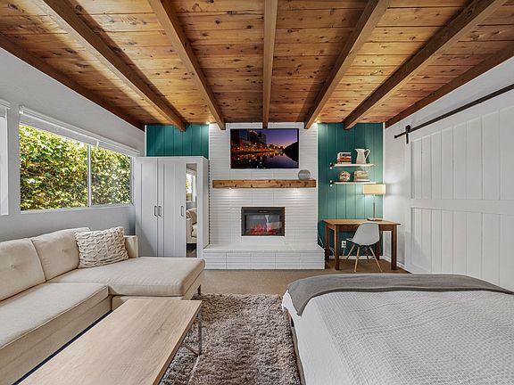 Studio guesthouse featuring open beam ceilings, fireplace, sofa, queen bed, wardrobe, 65" SmartTV and home office. Beautiful light from a wall of windows.