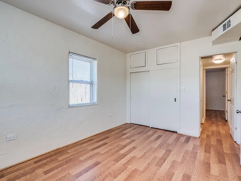 Bedroom 1 with ceiling fan and sliding closet. Entry to hallway leading to shared bathroom