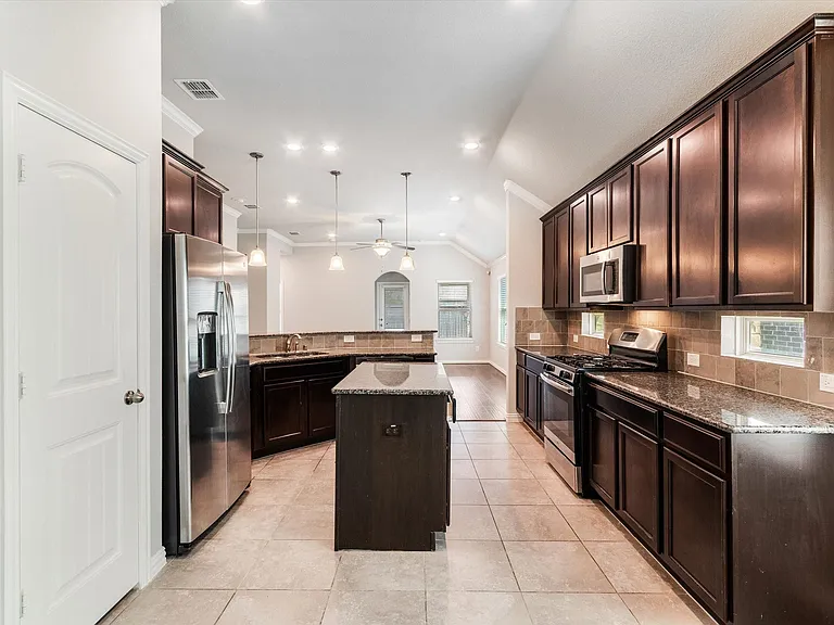 Kitchen featuring dark wood cabinetry, stainless steel appliances, granite countertops, and tile flooring