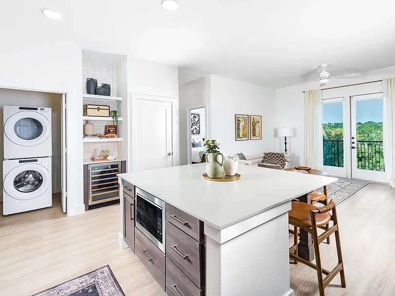 Open kitchen with a large island, built-in wine storage, and seamless flow to a bright living area with balcony views and in-home front loading washer and dryer.