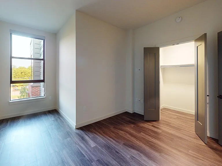 Spacious apartment bedroom with large closet and wood-style flooring.