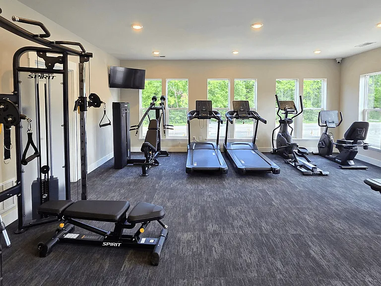 A spacious gym with a variety of equipment including treadmills, stationary bike, weights, and benches, located at the clubhouse at Greenwood Commons Apartments in Delaware, OH.