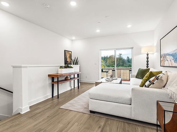 A modern and minimalist living room with a white couch, wooden console table, and a large window ove