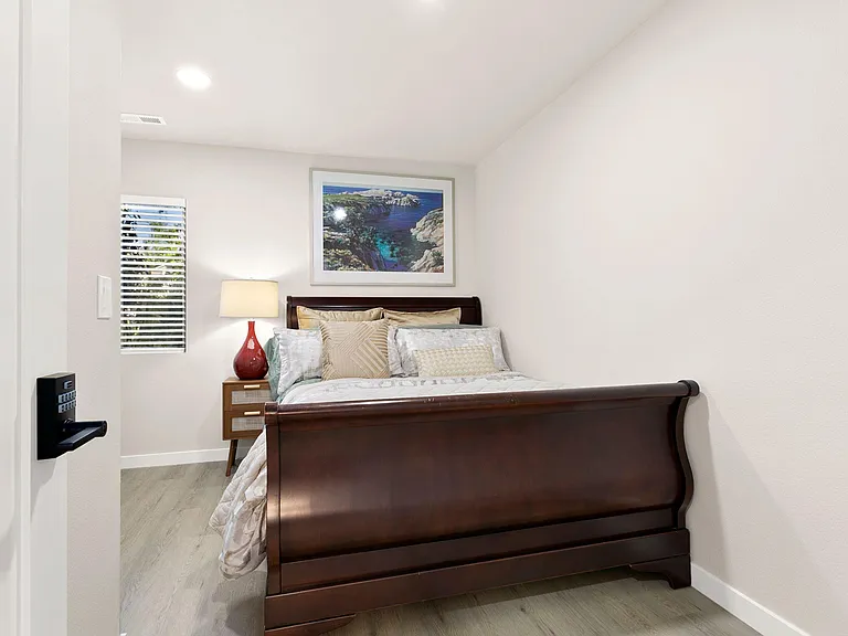 Private bedroom featuring a full-size bed, nightstand with lamp, and a window with blinds for light and privacy.