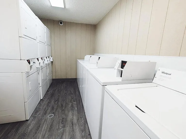 Modern laundry room featuring multiple efficient white washers and dryers, offering convenience and style with sleek wood flooring.